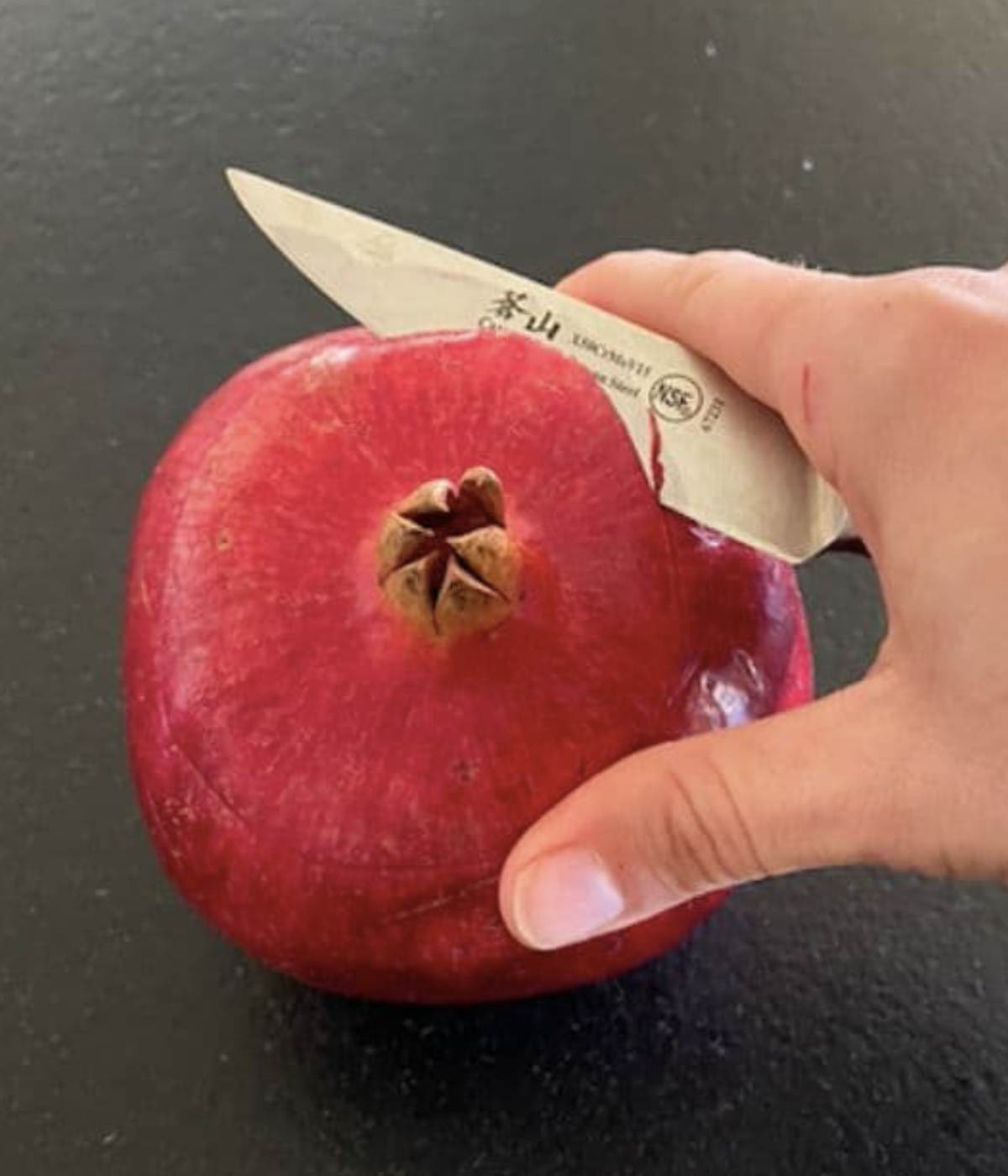 Opening pomegranate top with knife. 