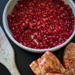 bowl of pomegranate arils (seeds) the empty rind on side with a wooden spoon