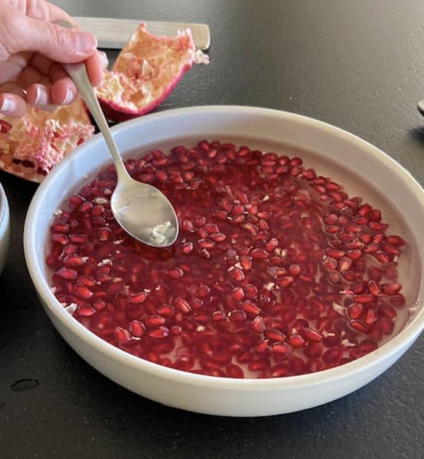 pomegranate arils in bowl with hand holding a spoon to remove the membrane pieces