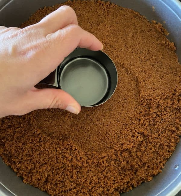hand packing crust into springform pan with the bottom of a measuring cup