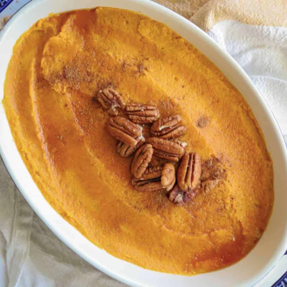 Whipped sweet potatoes topped with maple syrup and pecans in casserole dish.