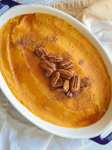 whipped sweet potatoes in casserole dish topped with pumpkin pie spice, pecans and a little maple syrup