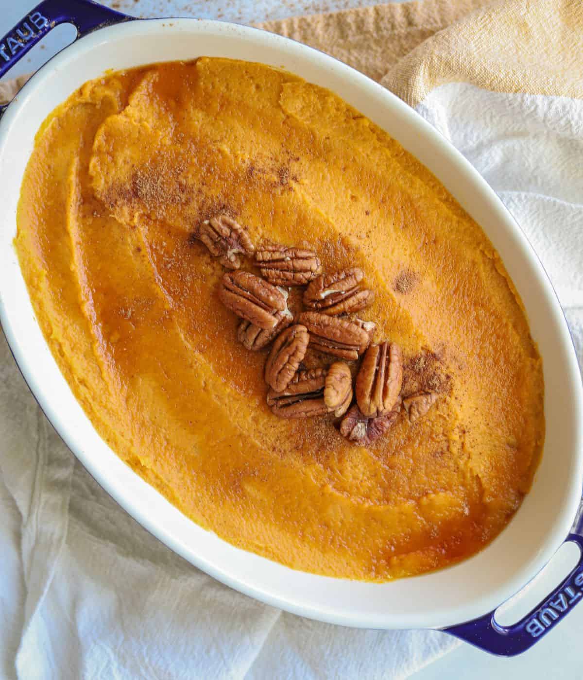 whipped sweet potatoes in casserole dish topped with pumpkin pie spice, pecans and a little maple syrup
