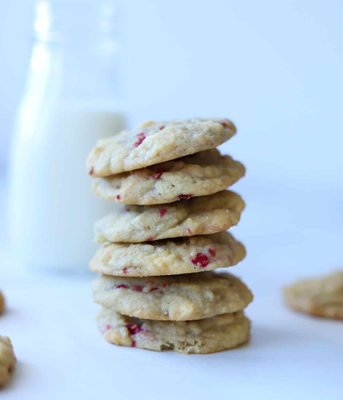 white chocolate raspberry cookies stacked on top of each other with milk in the background