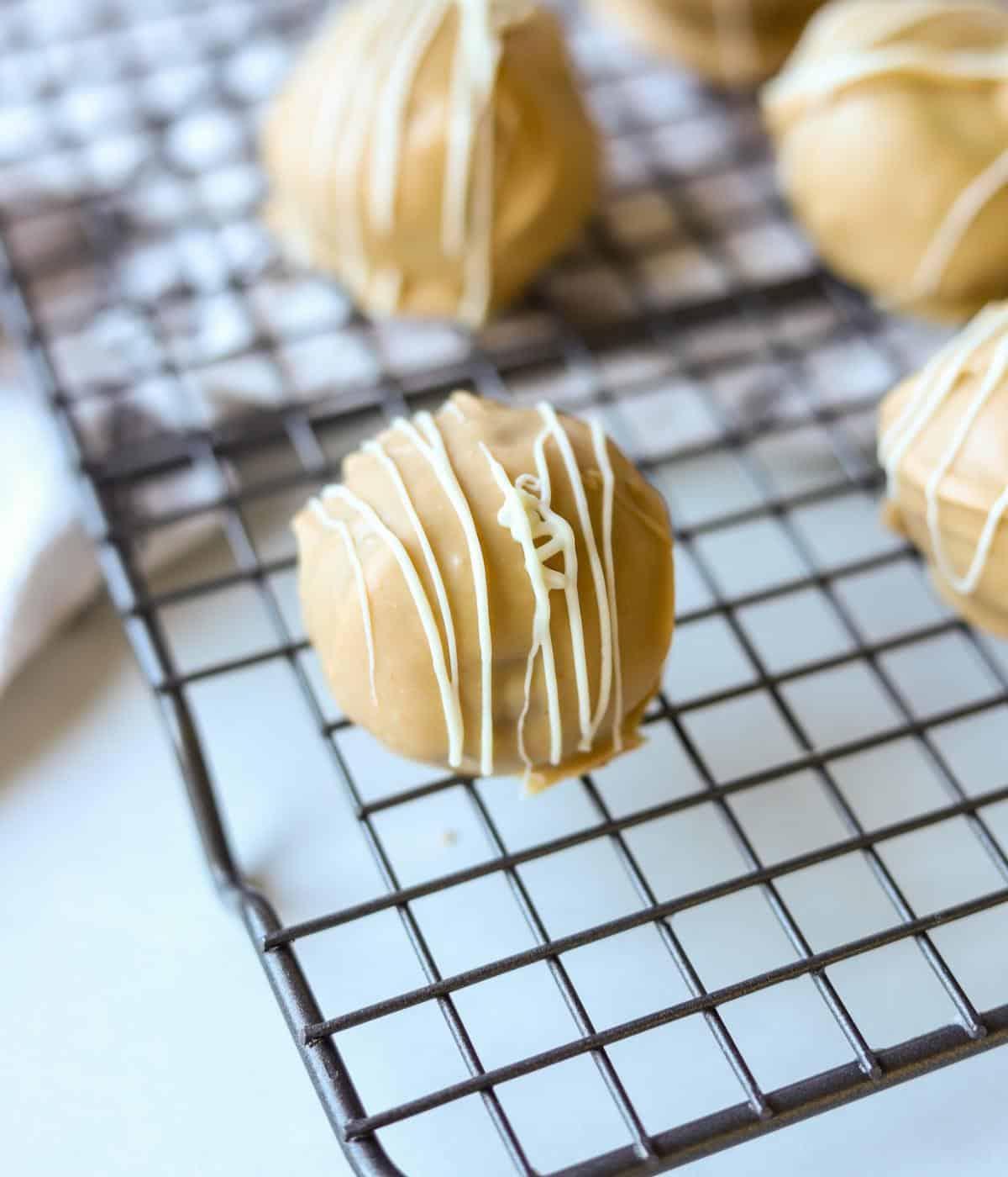 close up of truffle drizzled with white chocolate on baking rack