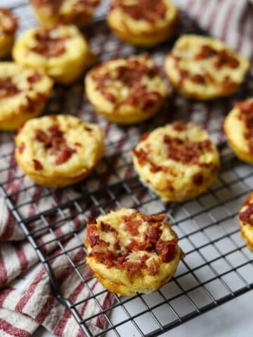 egg bites topped with bacon and melted cheese on a baking rack
