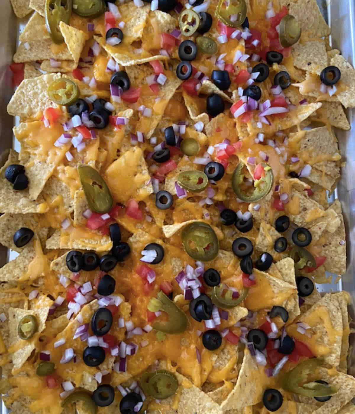 Cheesy nachos topped with veggies after coming out of the oven.