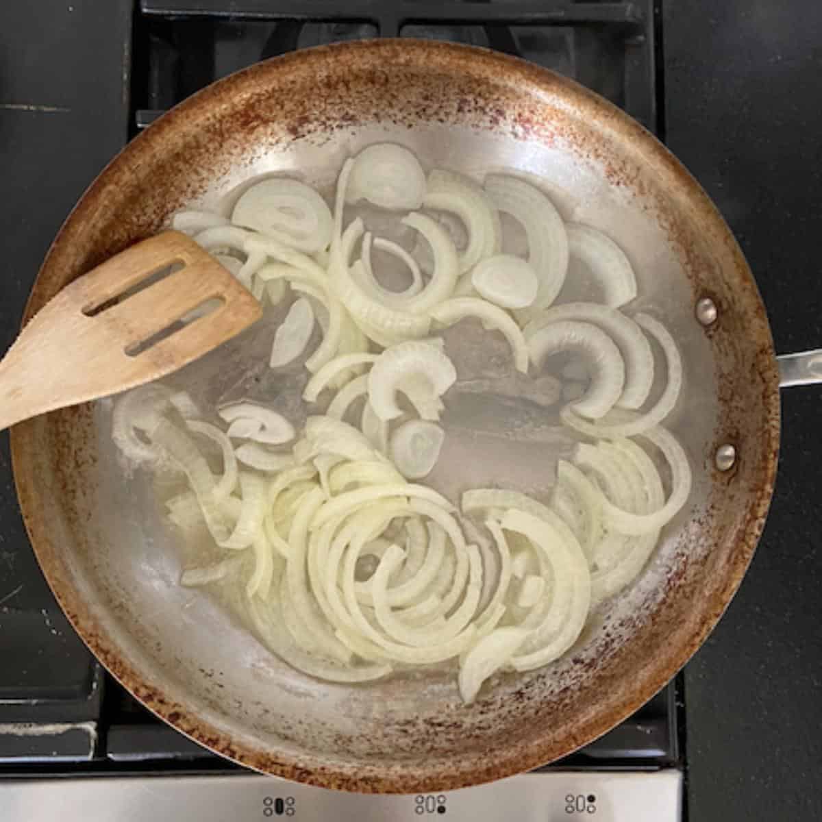 Caramelizing onions tossed into butter in pan with wooden spoon.