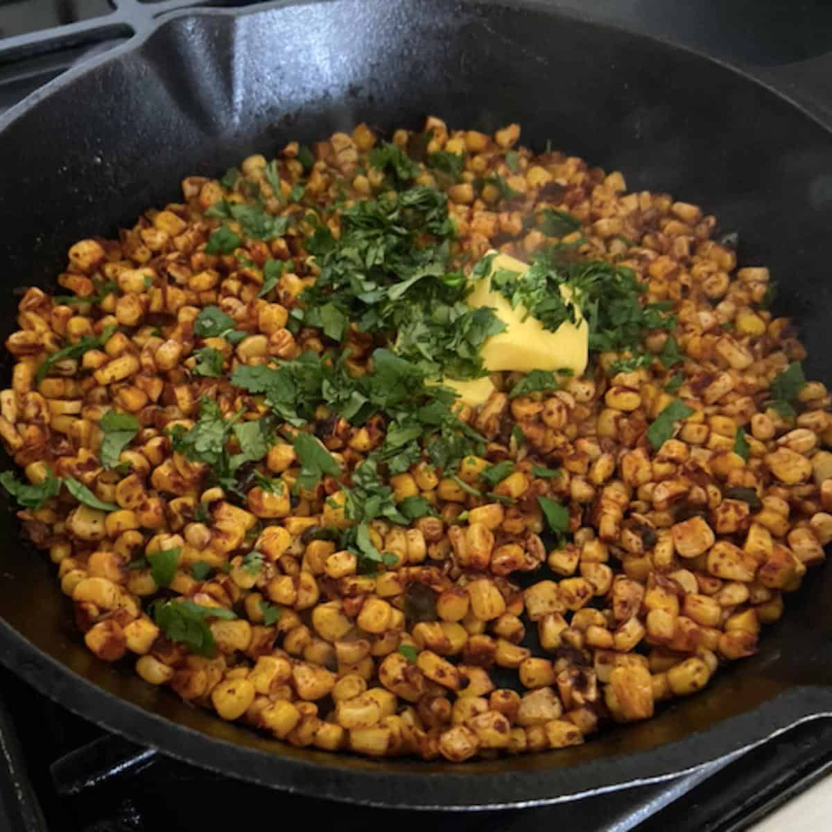 butter and cilantro added into skillet filled with charred corn