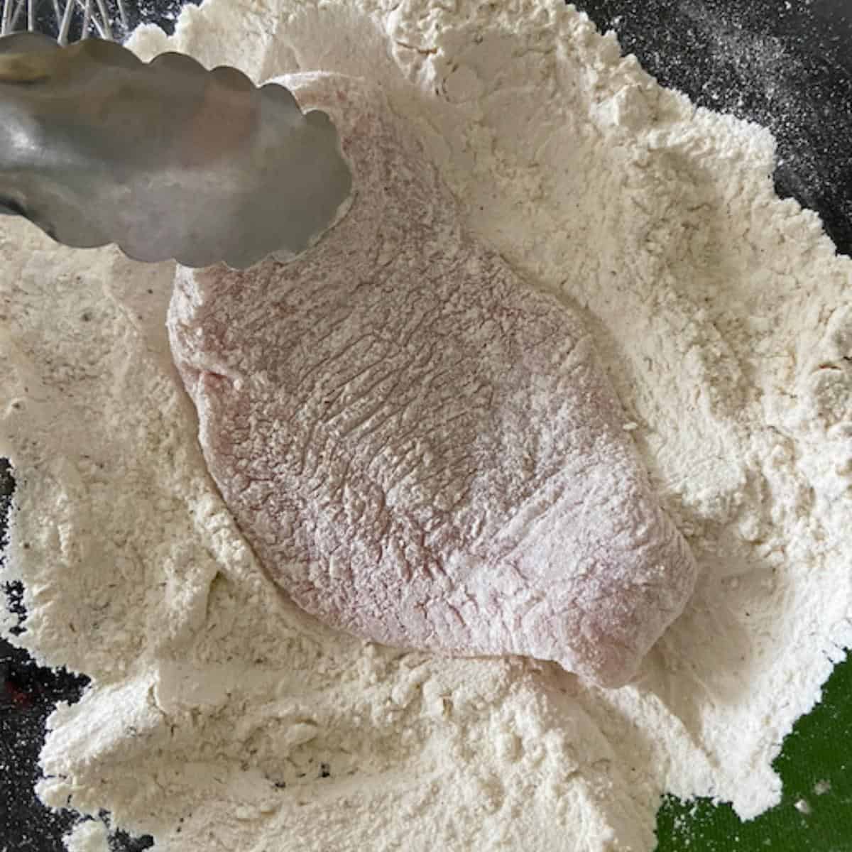 tongs coating chicken in flour mixture