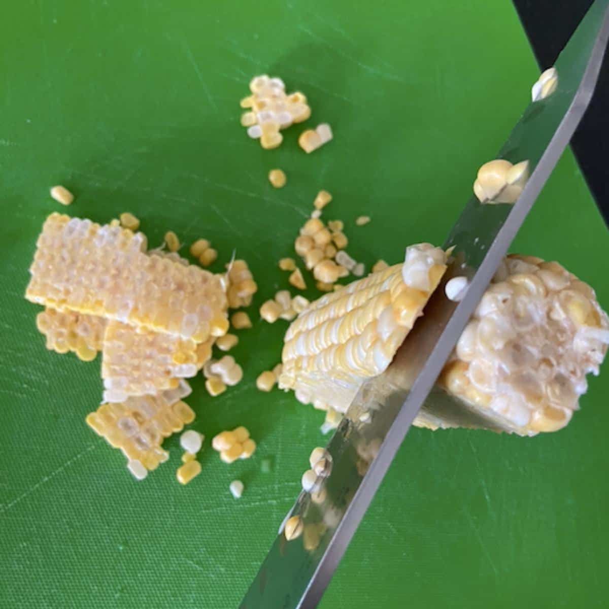 knife slicing corn off the cob on a cutting board