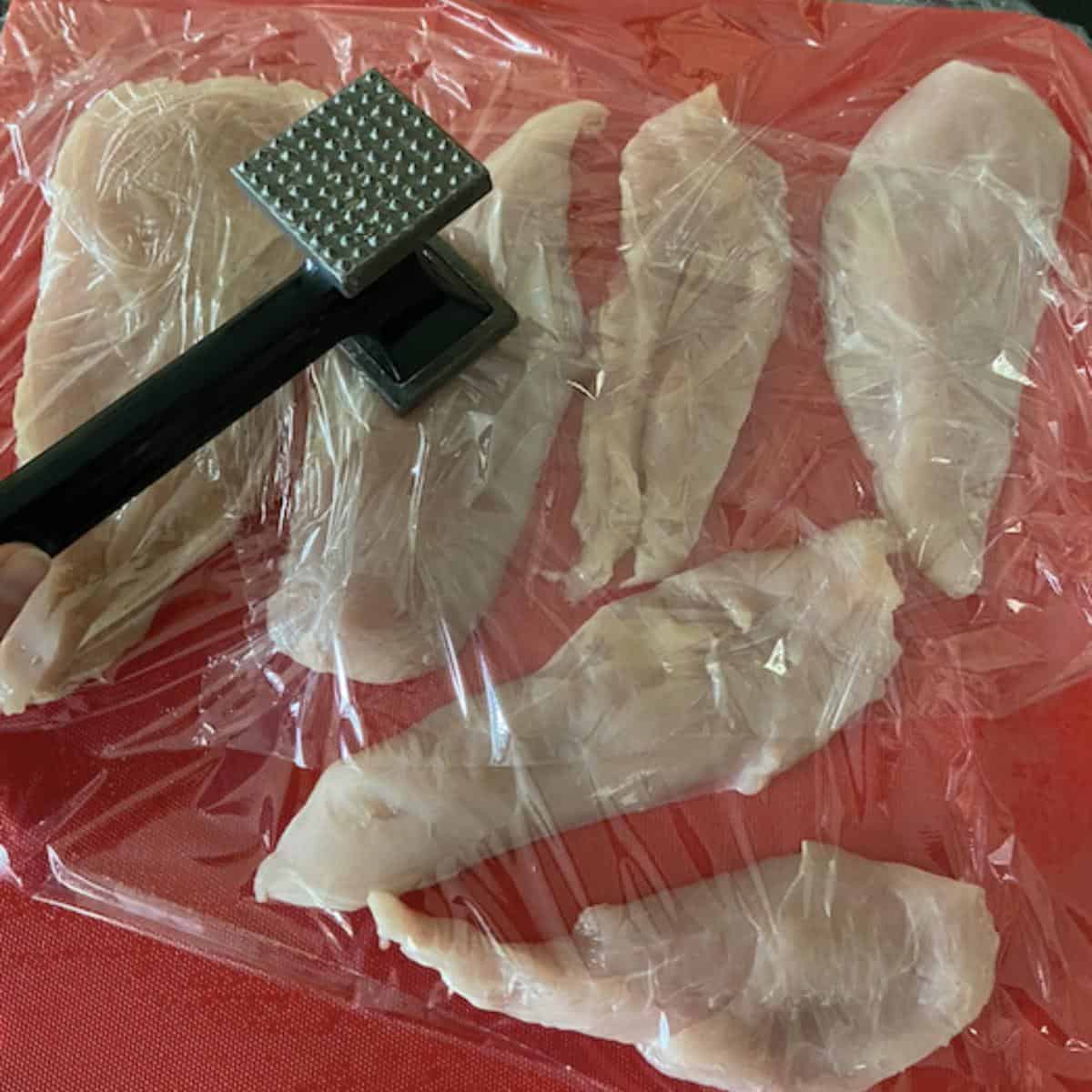 mallet pounding chicken breast on cutting board