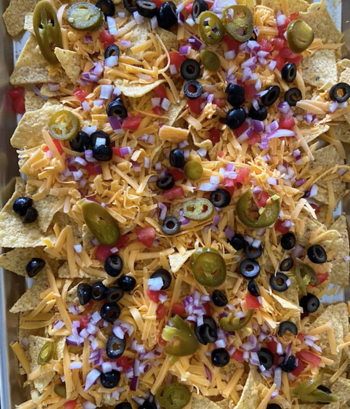 nachos on cookie sheet with cheese and veggies ready to bake in the oven