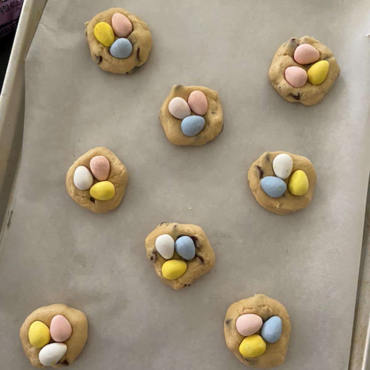 chocolate chip cookies with 3 mini eggs on each cookie spread out on parchment lined cookie sheet
