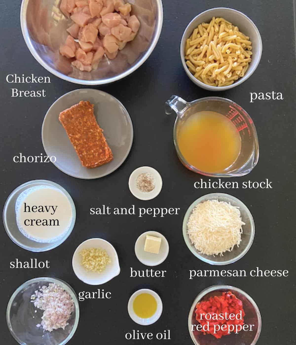 ingredients for chicken chorizo pasta on black countertop with text added