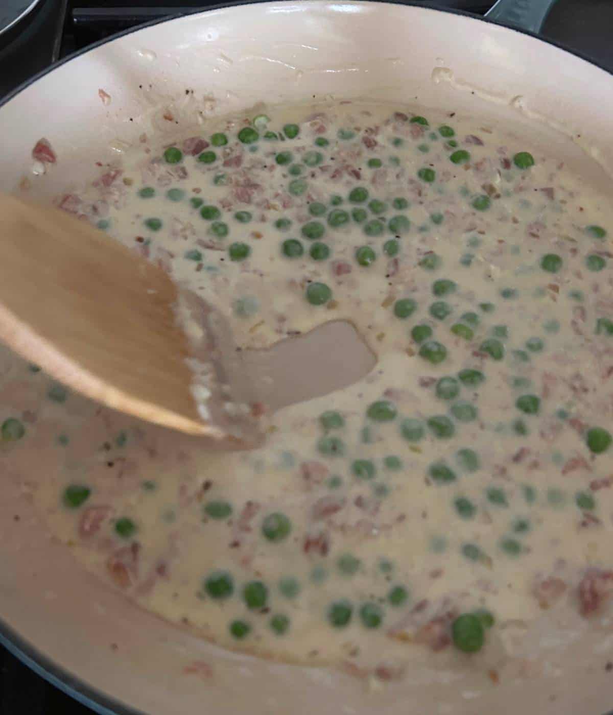 Creamy sauce in skillet with peas.