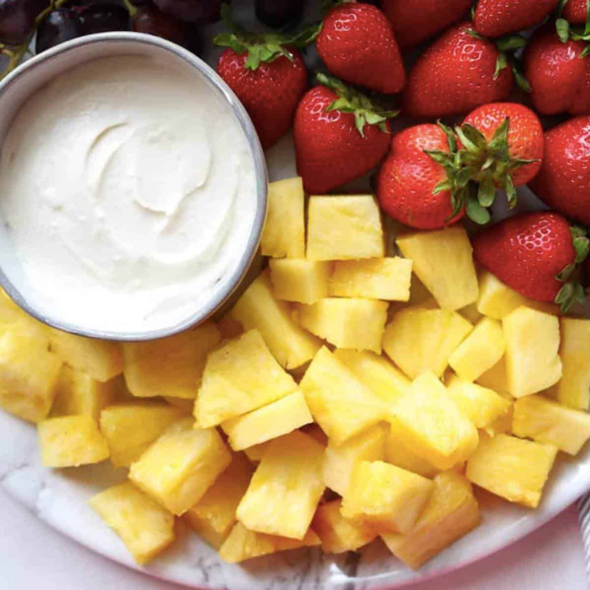 Marshmallow fluff fruit dip with strawberry and pineapple on platter.