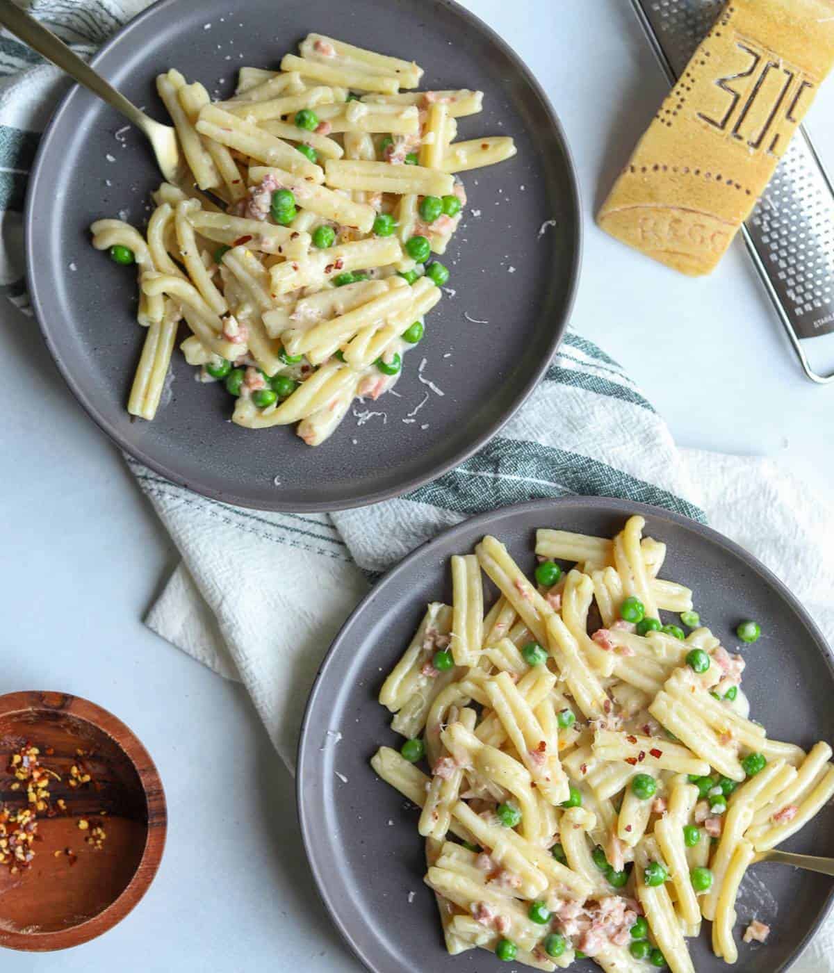 Pancetta and pea pasta on gray plates topped with parmesan.