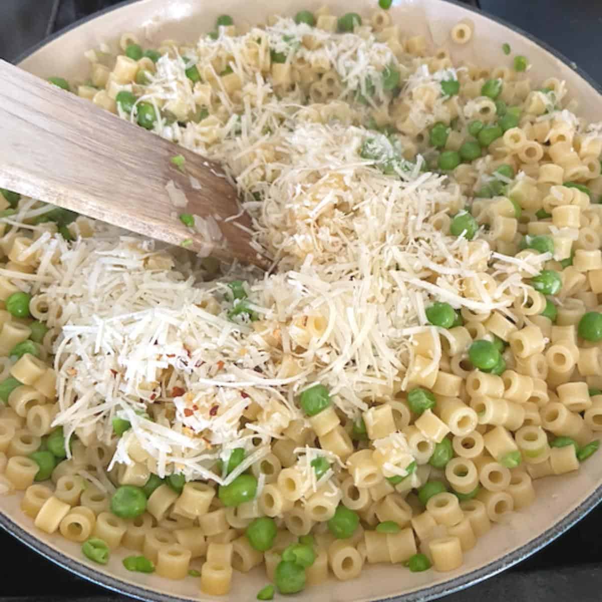 wooden spoon stirring cheese into pasta and peas