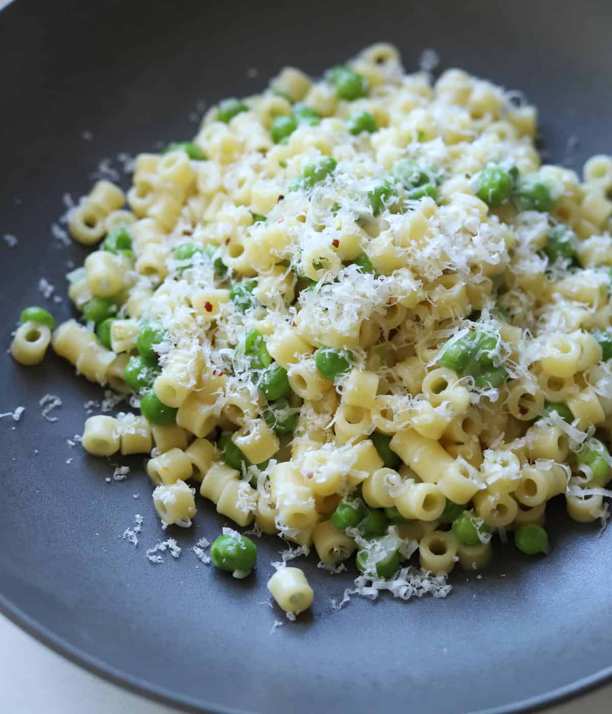 close up of finished pasta and peas covered with parmesan cheese on gray plate