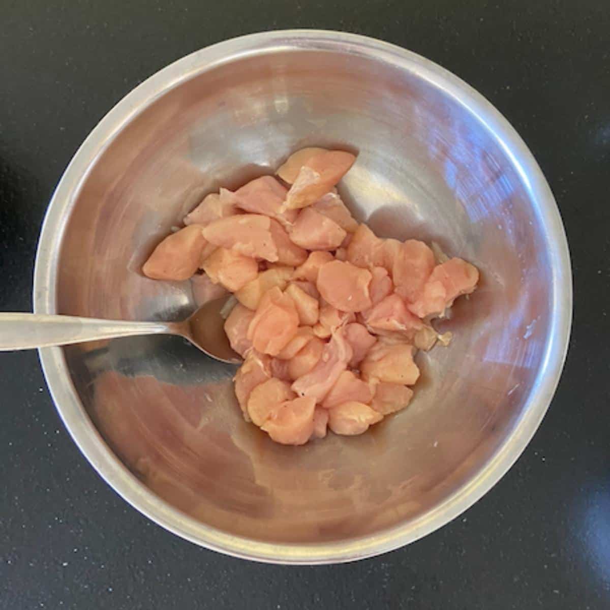 chicken breast cut into cubes in a stainless bowl with salt and pepper