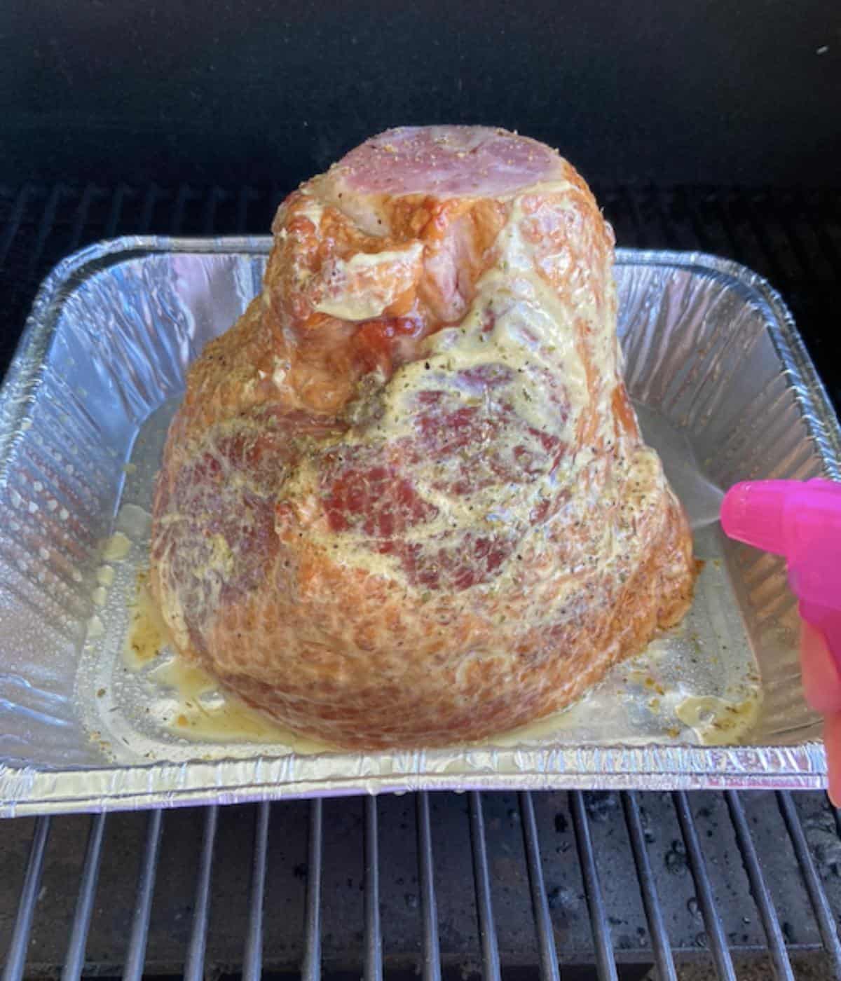ham in baking tray on traeger being sprayed with pineapple juice