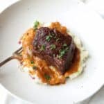 beef short ribs over mashed potatoes and gravy in white bowl with fork