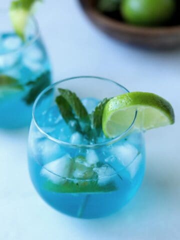 blue mojito in wine glass topped with mint and lime