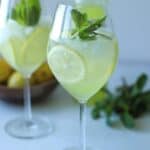 two wine glasses full of limoncello spritz with lemons and mint in the glasses