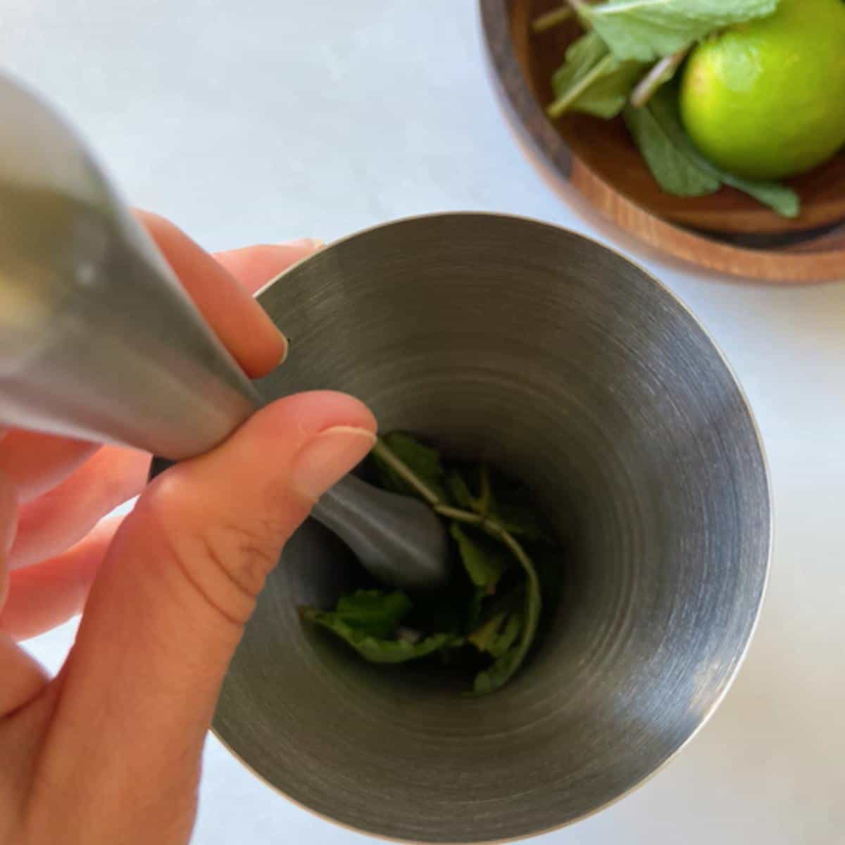 hand muddling mint in stainless steel shaker