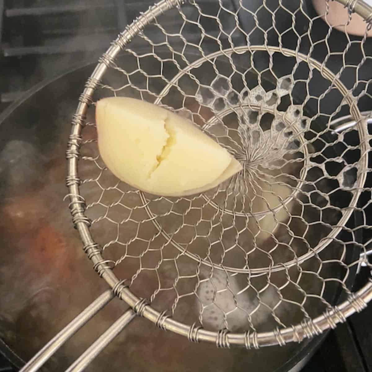 colander spoon showing potato that has been cooked entirely
