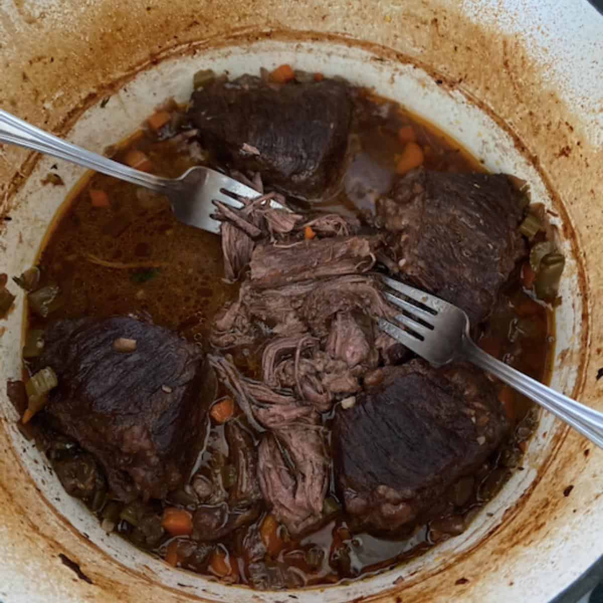 Forks pulling apart short ribs in dutch oven.