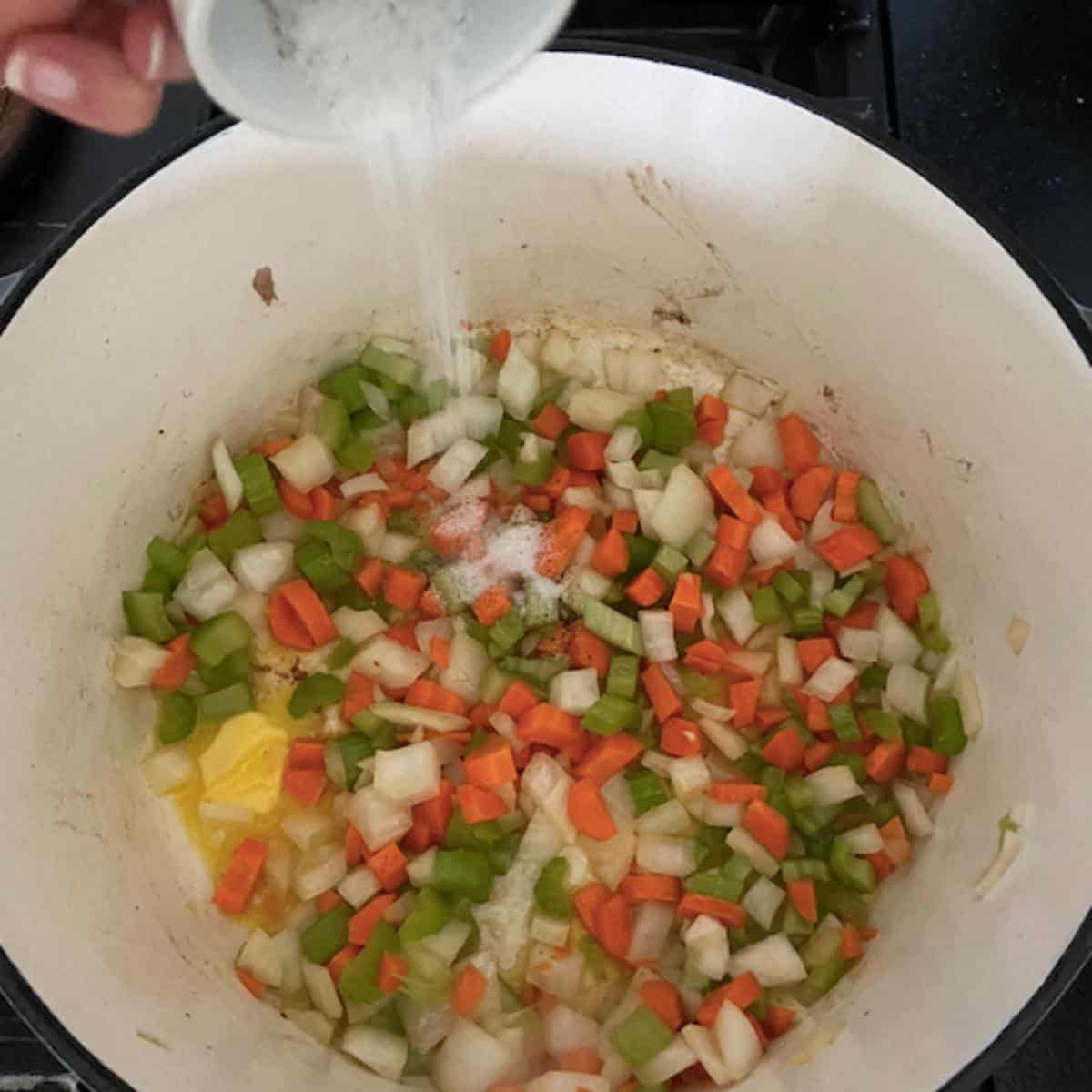 vegetables softening in dutch oven and hand pouring in salt and pepper