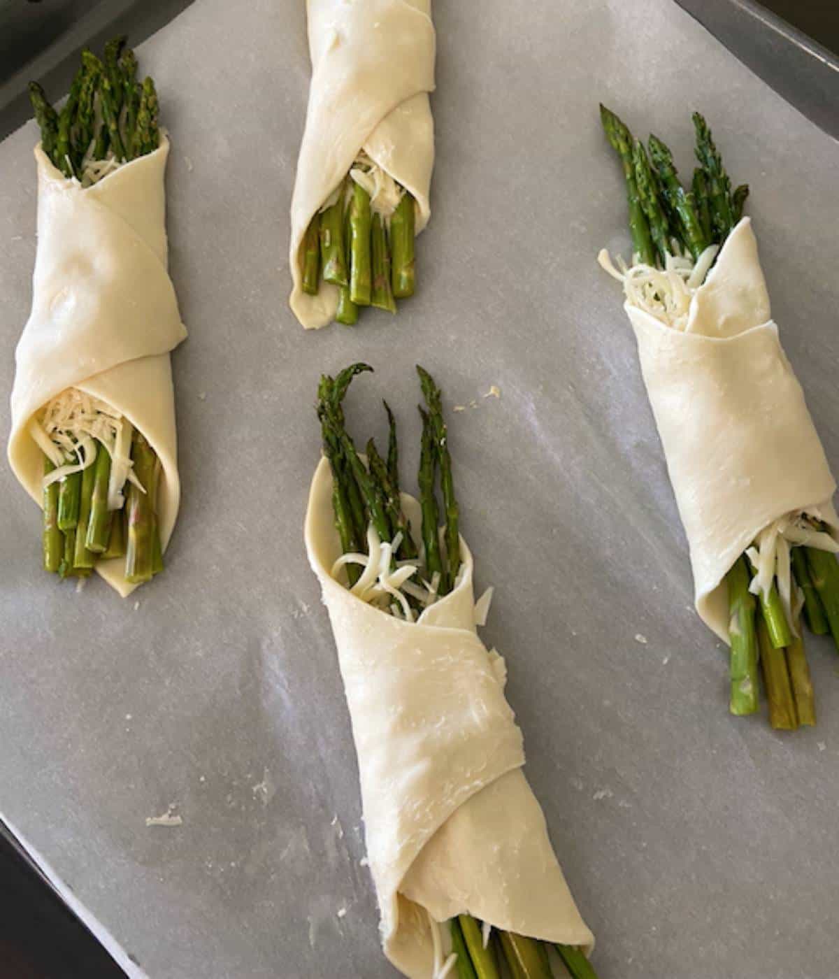 Asparagus puff pastry wrapped up on cookie sheet lined with parchment paper.