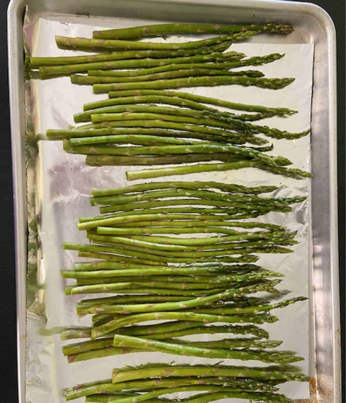 Asparagus with olive oil, salt and pepper on cookie sheet with foil.