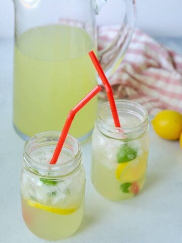 Two mason jars full of lemonade with a pitcher next to them.