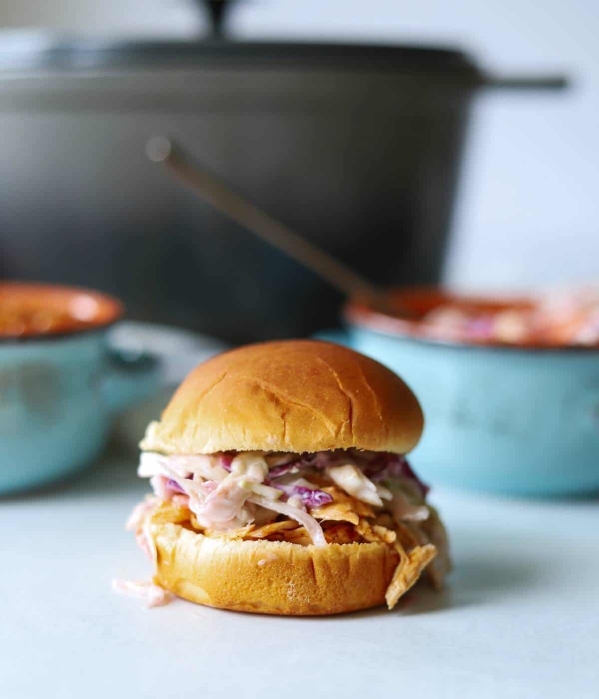 BBQ chicken sandwich topped with slaw with dutch oven in background.