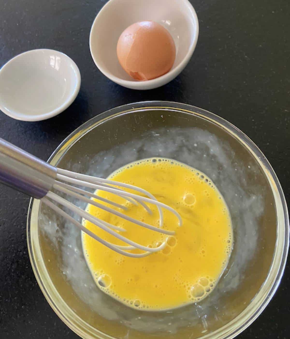 Egg wash in glass bowl with whisk.