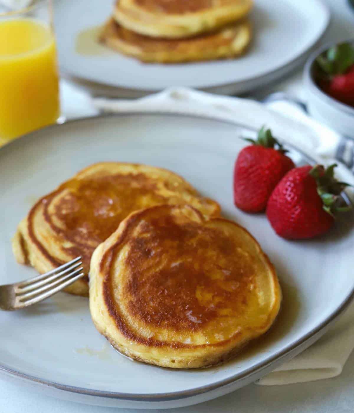 Pancakes covered in syrup on a gray plate with side of strawberries.