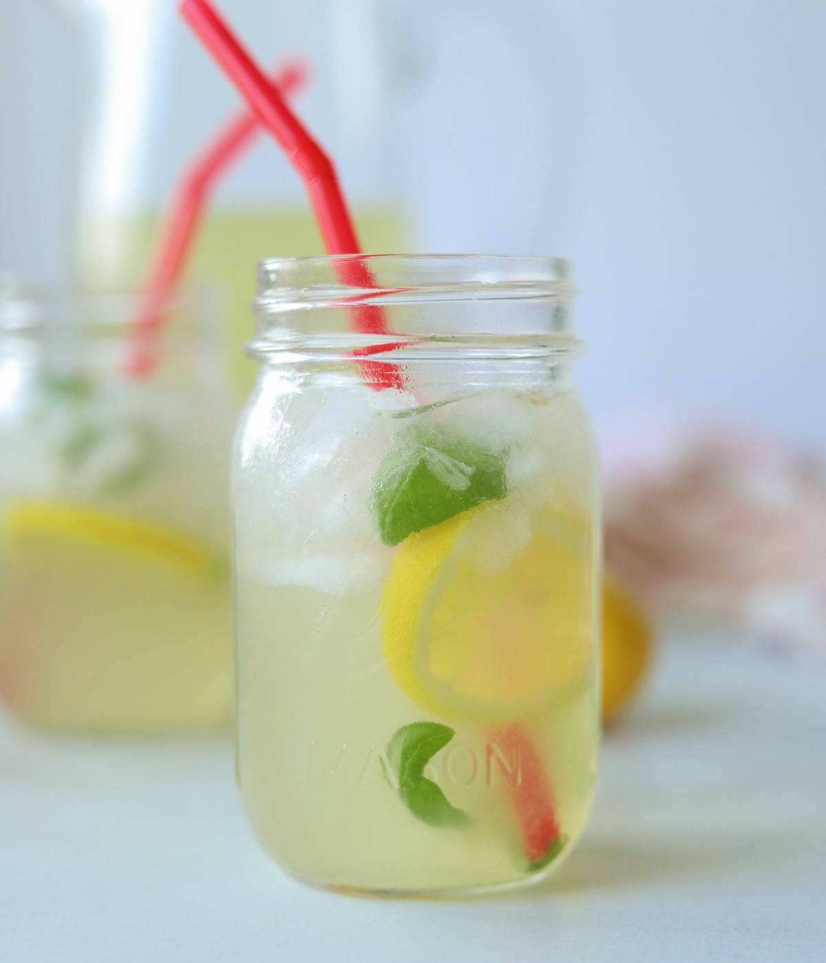 Glass of basil lemonade in mason jar with red straw.
