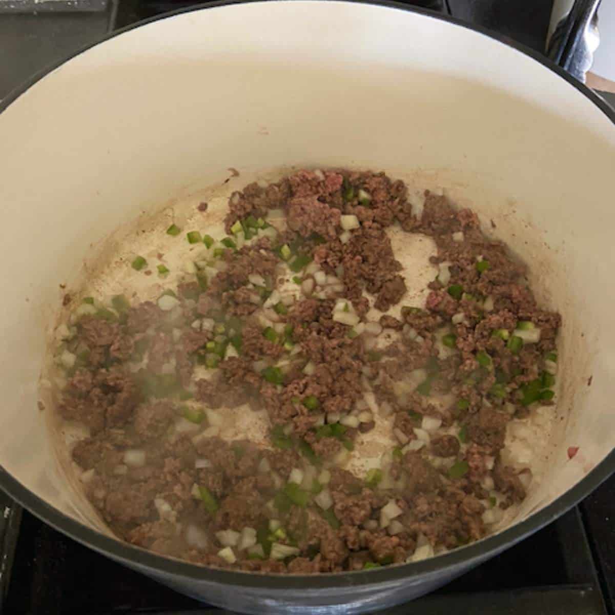 Ground beef with peppers and onions cooking in dutch oven.