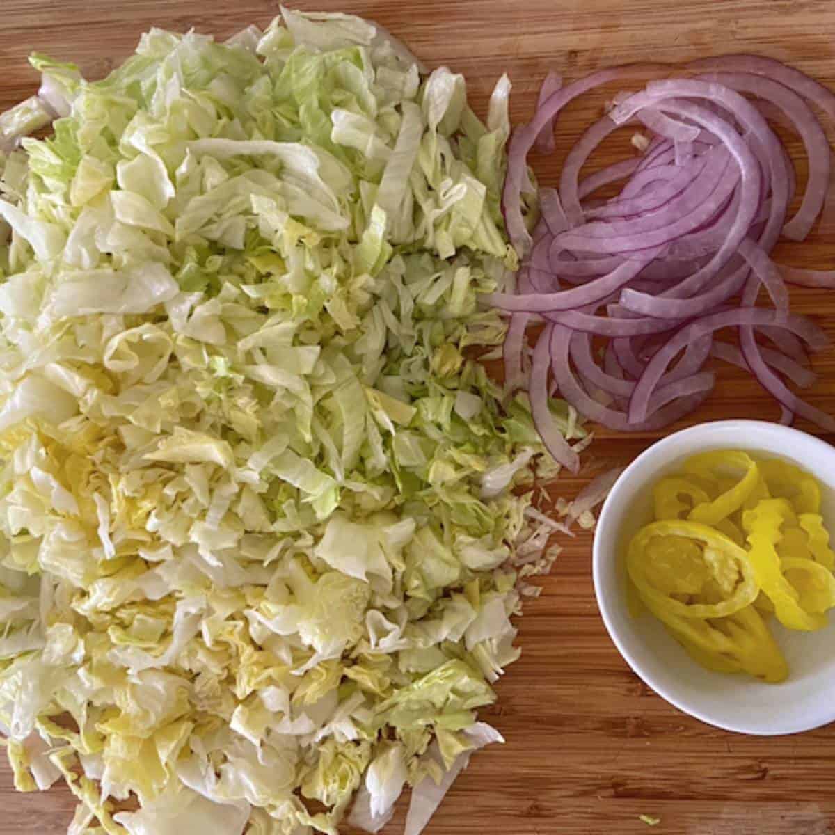 Chopped lettuce, onion and banana peppers on cutting board.