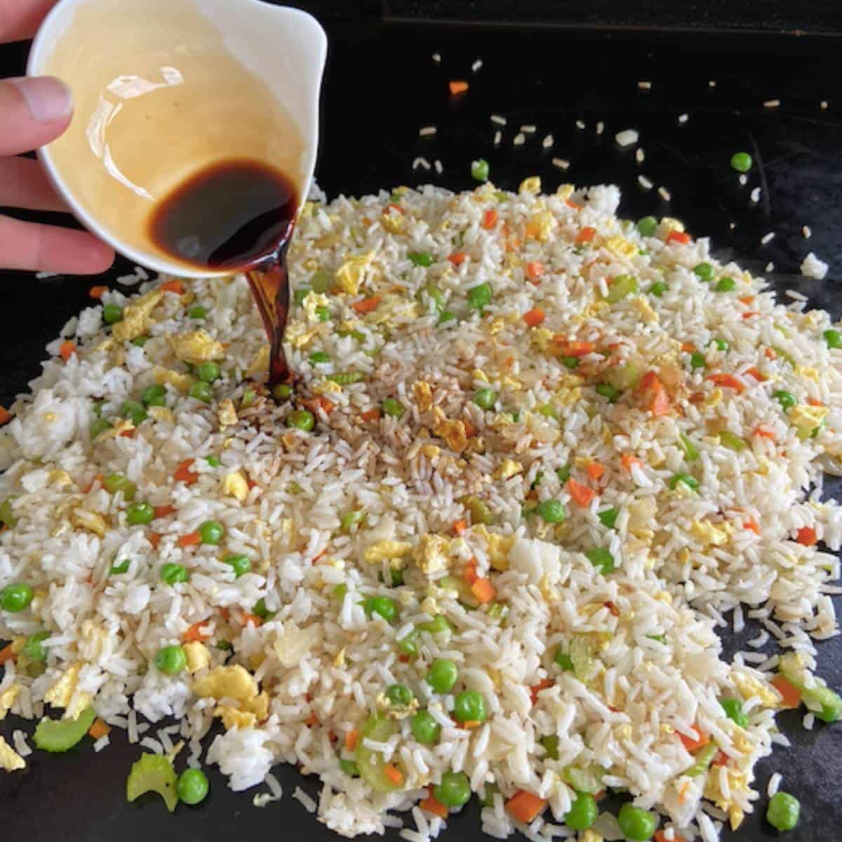 Hand pouring soy sauce over fried rice.