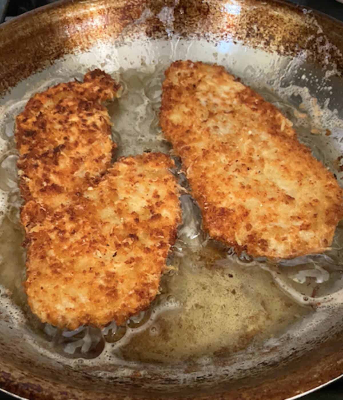 Chicken romano frying in oil in stainless steel pan.