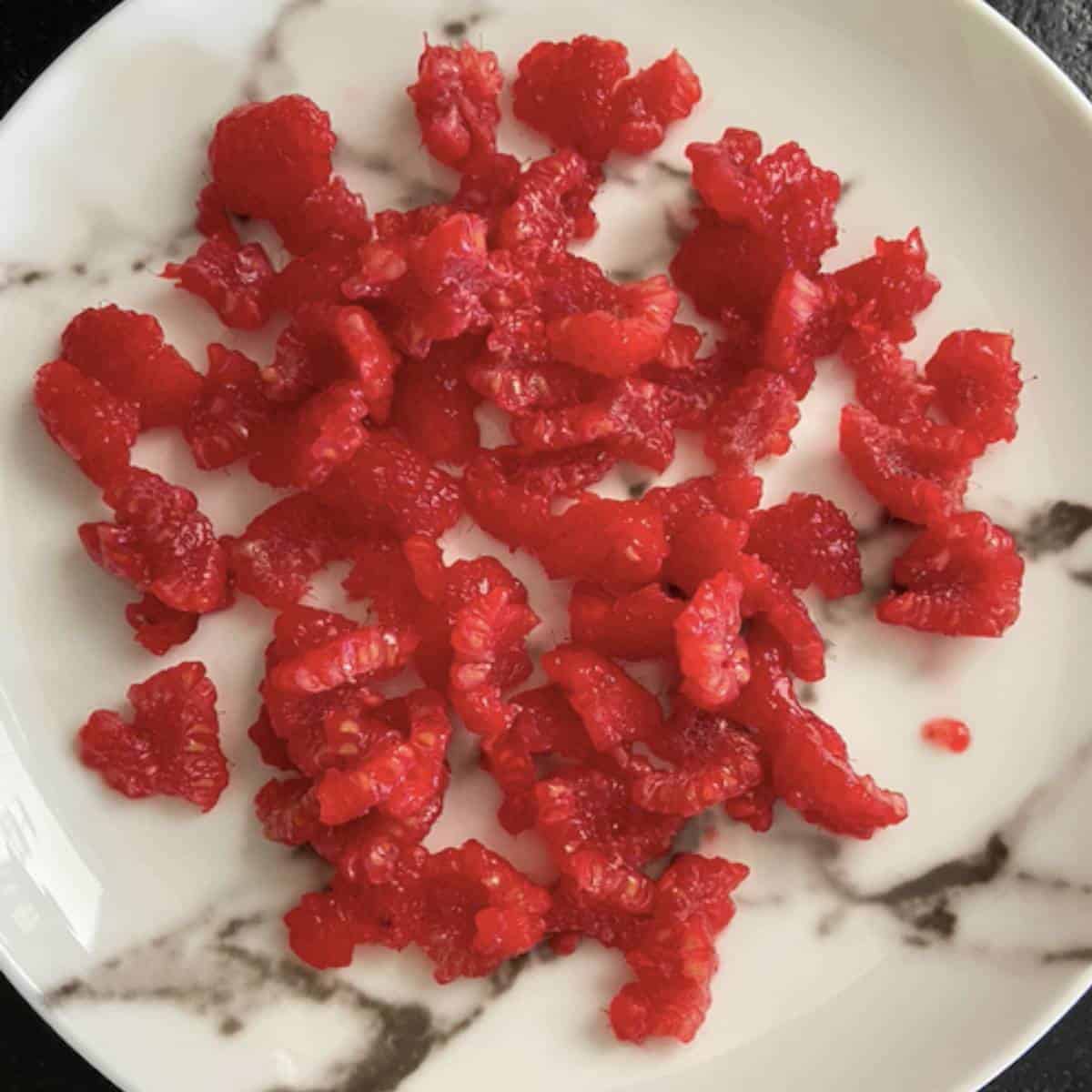 Raspberries ripped into smaller pieces on plate.