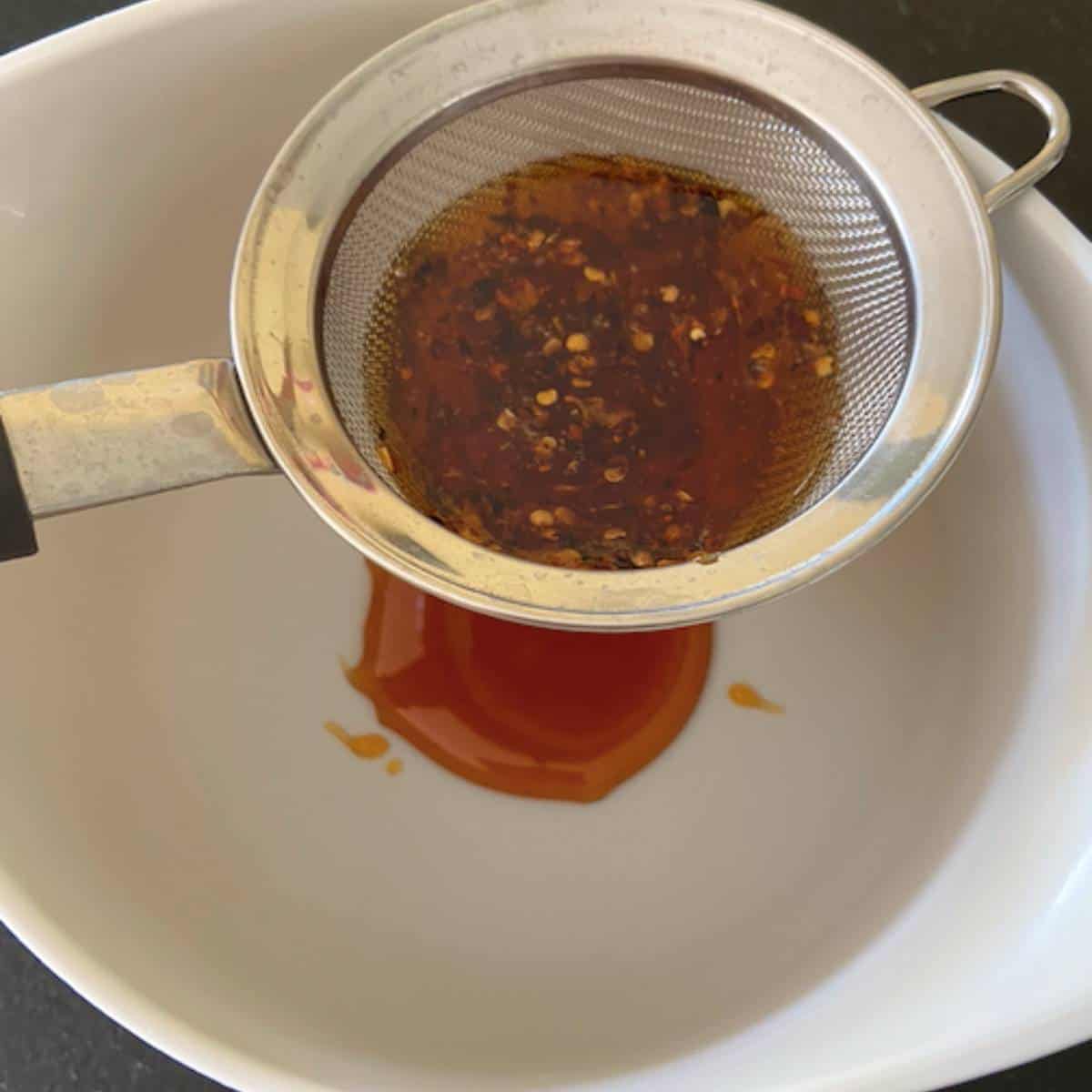 Straining infused honey in strainer with bowl underneath.