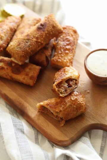 BBQ pulled pork egg rolls on wooden platter with side of ranch.