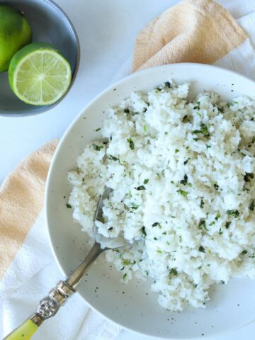 Coconut lime rice topped with cilantro in bowl with side of limes.