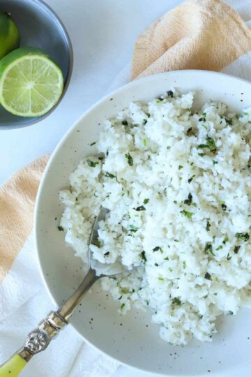 Coconut lime rice topped with cilantro in bowl with side of limes.
