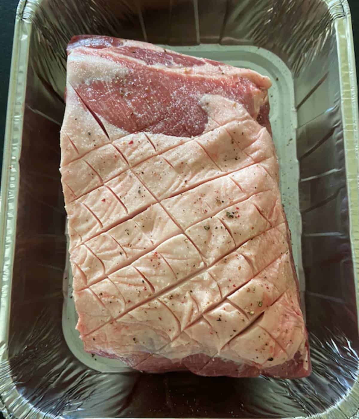Scored pork butt in tin foil pan.